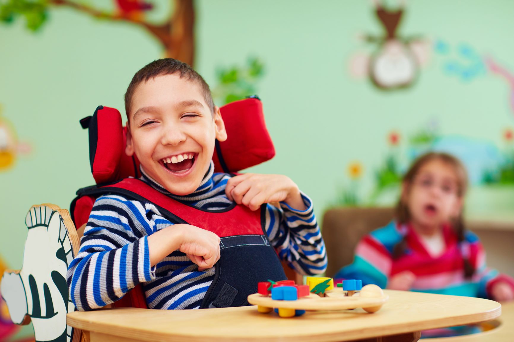 Iloinen, nauravainen vammainen poika istuu tuolissa ja leikkii palikoilla.