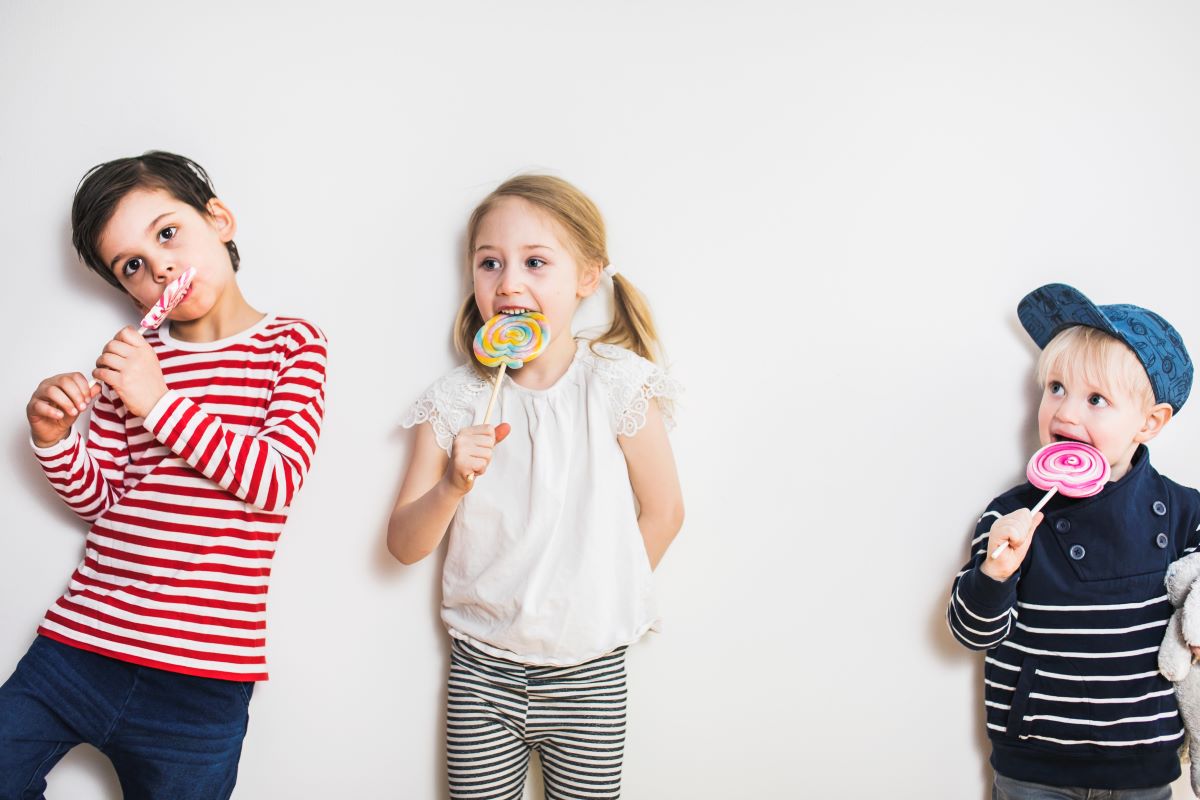 Eri-ikäiset lapset syövät yhdessä värikkäitä tikkukaramelleja.