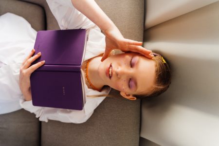 Nuori tyttö lukee violettia kirjaa sohvalla.