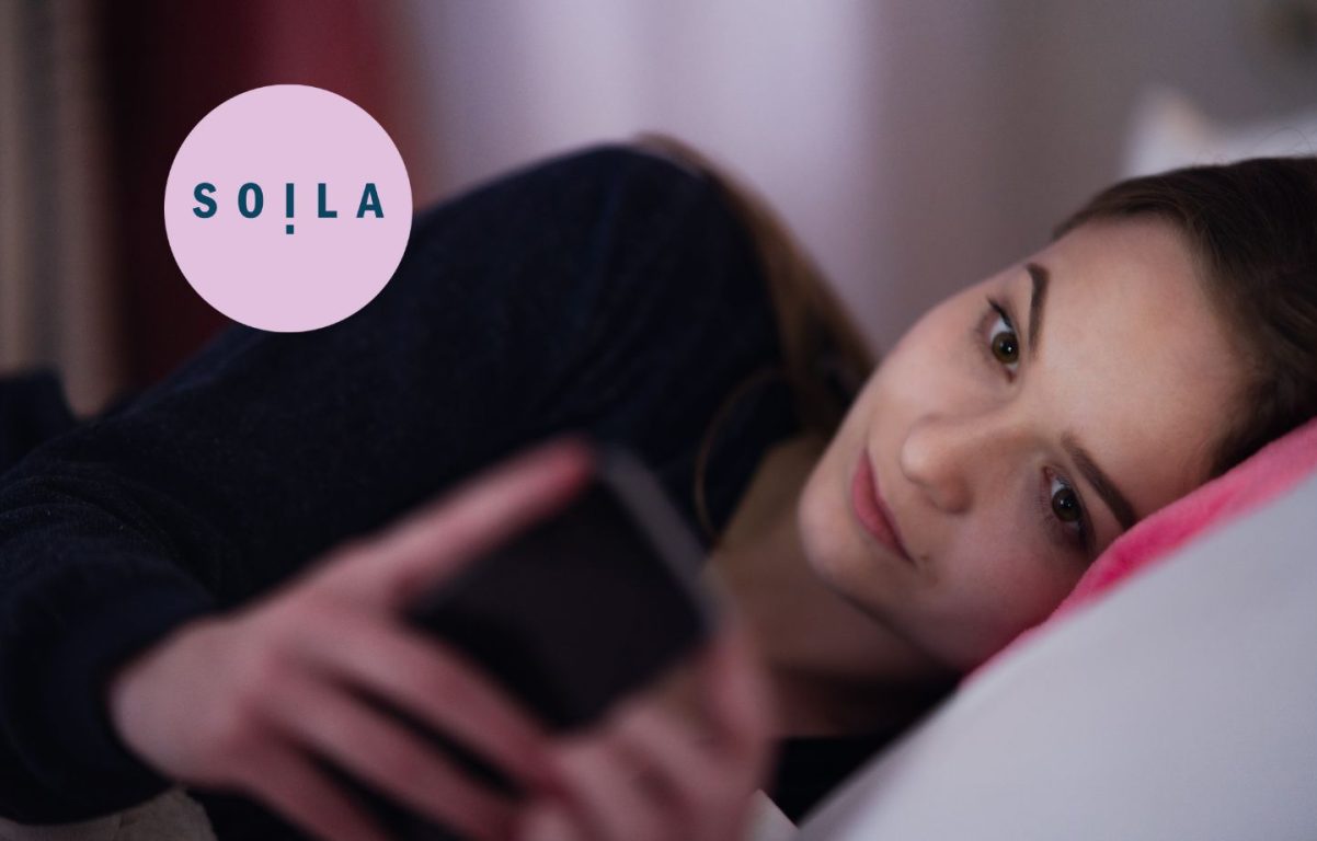 Nuori tyttö makaa sängyssä kyljellään selaten puhelinta.