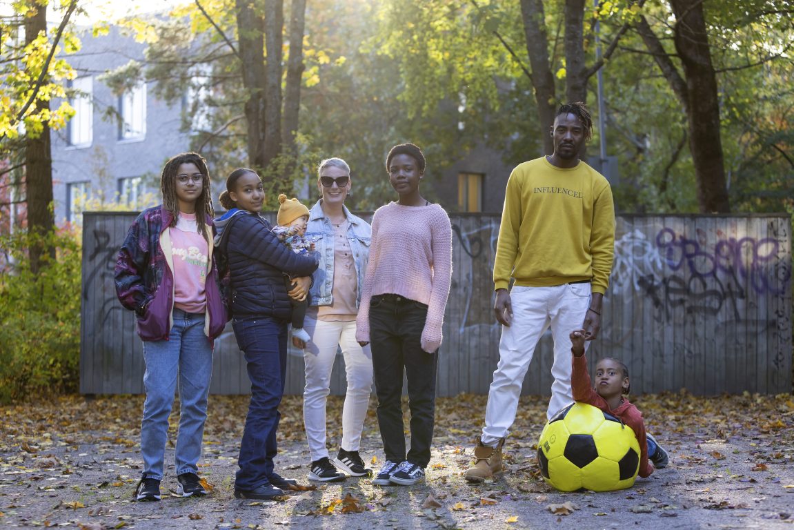 Seitsemänhenkinen perhe poseeraa puistossa kameralle.