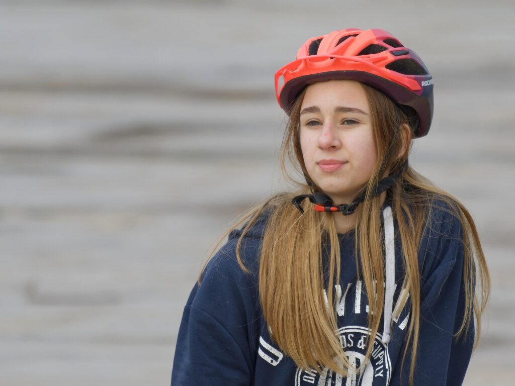 Nuori tyttö istuu maassa pyöräilykypärä päässään.